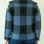 A person shown from the back wearing a blue and dark green plaid wool coat over dark blue jeans, against a plain off-white background.
