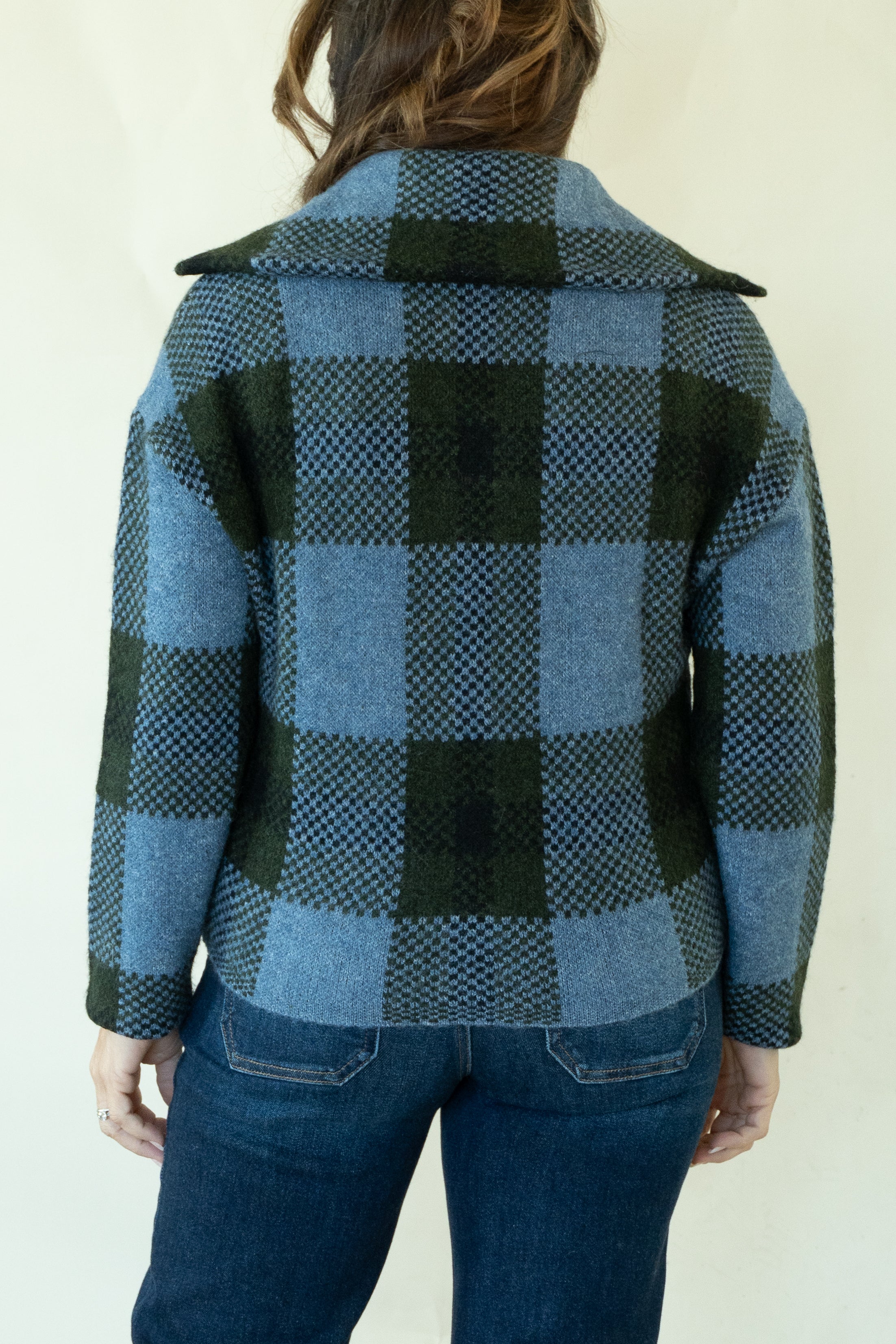 A person shown from the back wearing a blue and dark green plaid wool coat over dark blue jeans, against a plain off-white background.