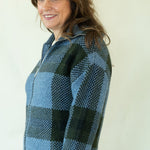 Woman wearing blue and green buffalo check zip front cardigan with dark jeans and ankle boots