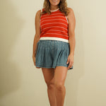 Woman wearing a red and white striped tank top and denim skirt against a beige wall.