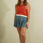 Woman wearing a red striped sleeveless top and denim skirt against a plain background