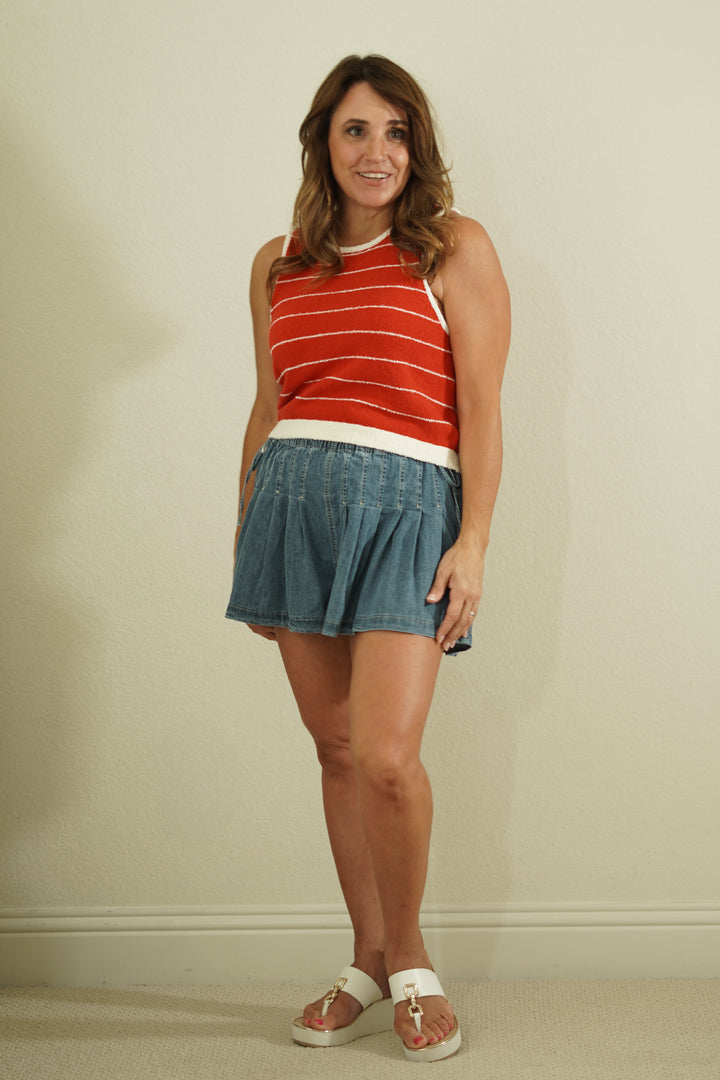 Woman wearing a red striped sleeveless top and denim skirt against a plain background