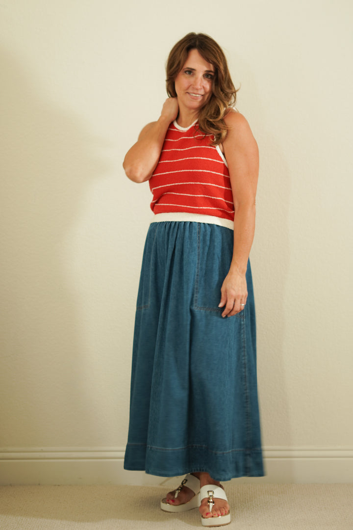 Woman wearing a red striped top and blue denim skirt against a plain background