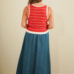 Person wearing a red and white striped tank top and blue denim skirt against a beige wall.