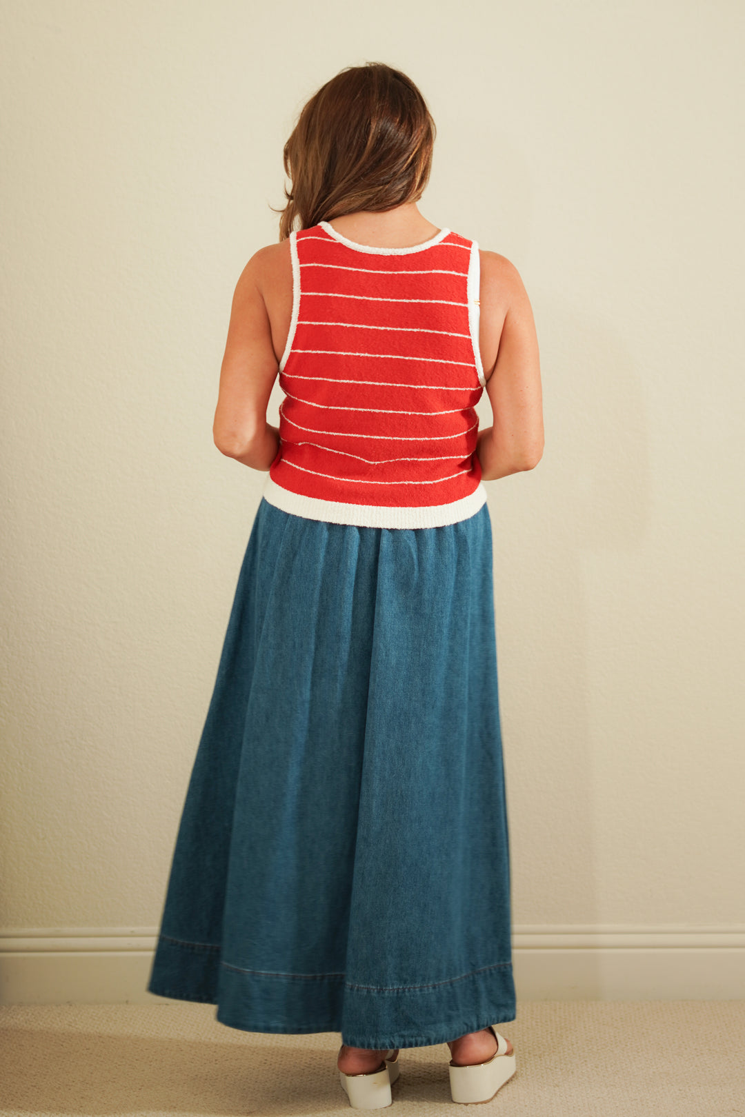 Person wearing a red and white striped tank top and blue denim skirt against a beige wall.