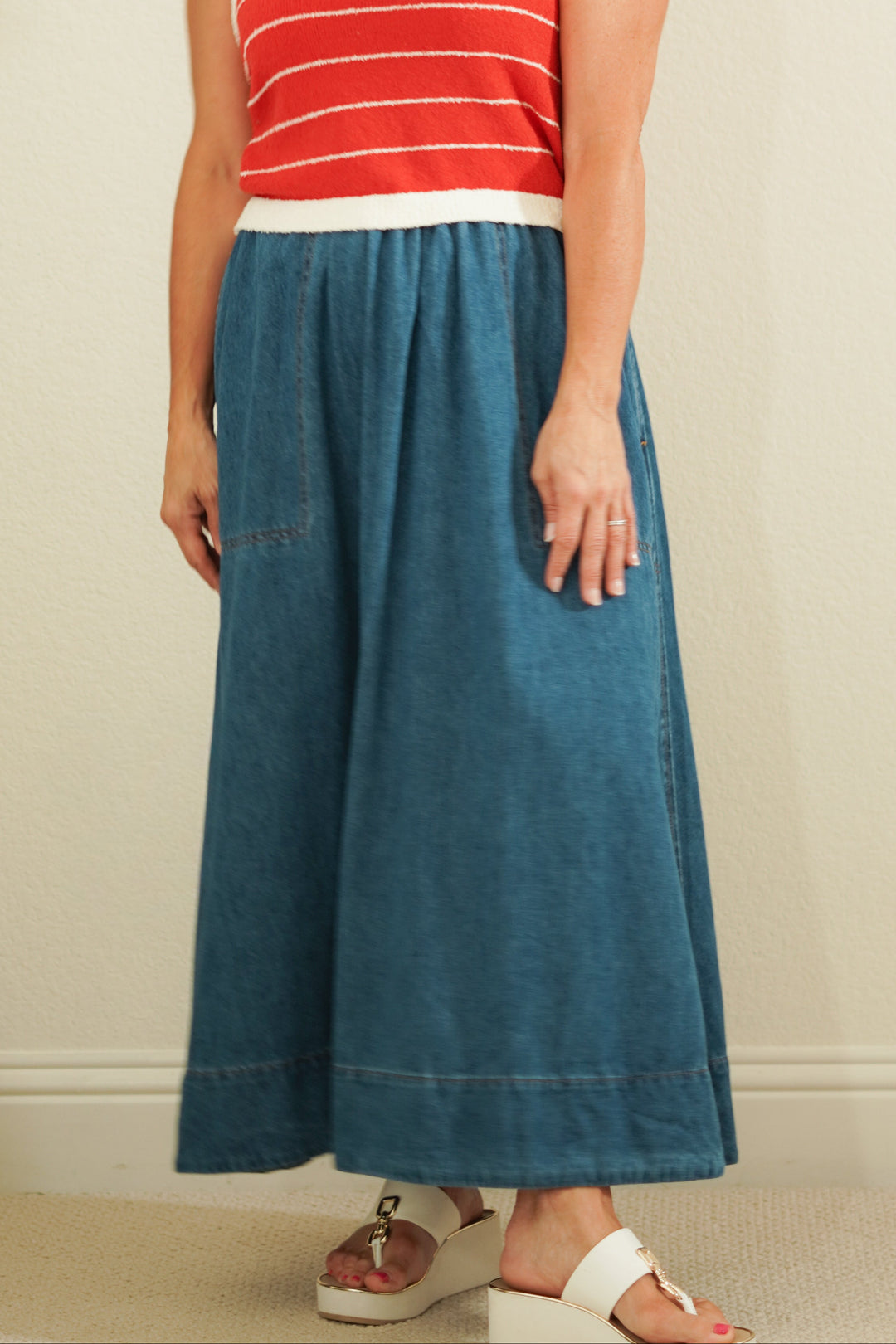 Woman wearing a red and white striped sleeveless top and blue denim skirt against a plain background