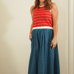 Woman wearing a red striped sleeveless top and blue denim skirt against a plain background