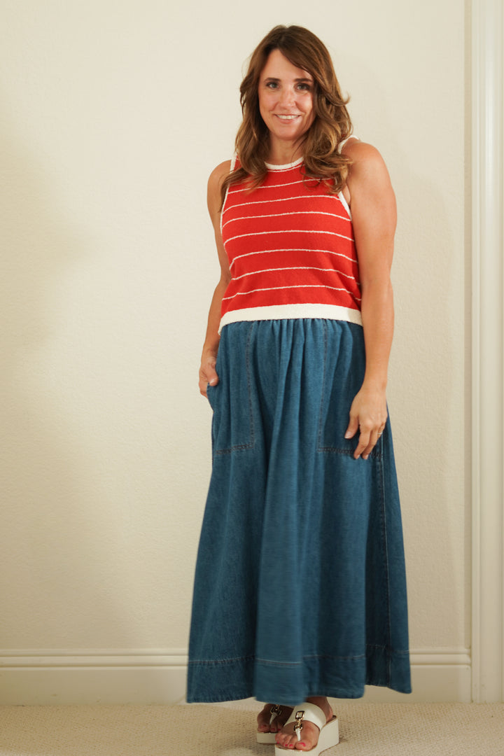Woman wearing a red striped sleeveless top and blue denim skirt against a plain background