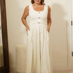 Woman in a white dress standing in front of a mirror in a room with beige walls.