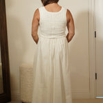 Person wearing a white dress standing in front of a mirror in a room.