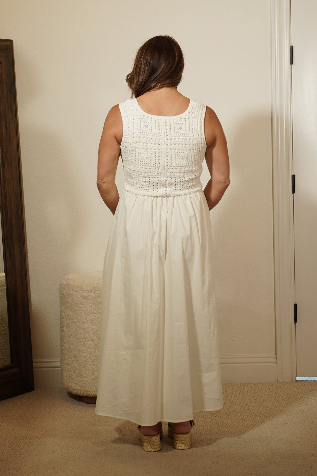 Person wearing a white dress standing in front of a mirror in a room.