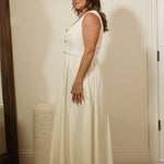Woman in a white dress standing in a room with a mirror on the wall.