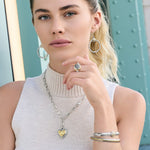 Woman wearing silver hoop earrings, a ring, and bracelets with a neutral background