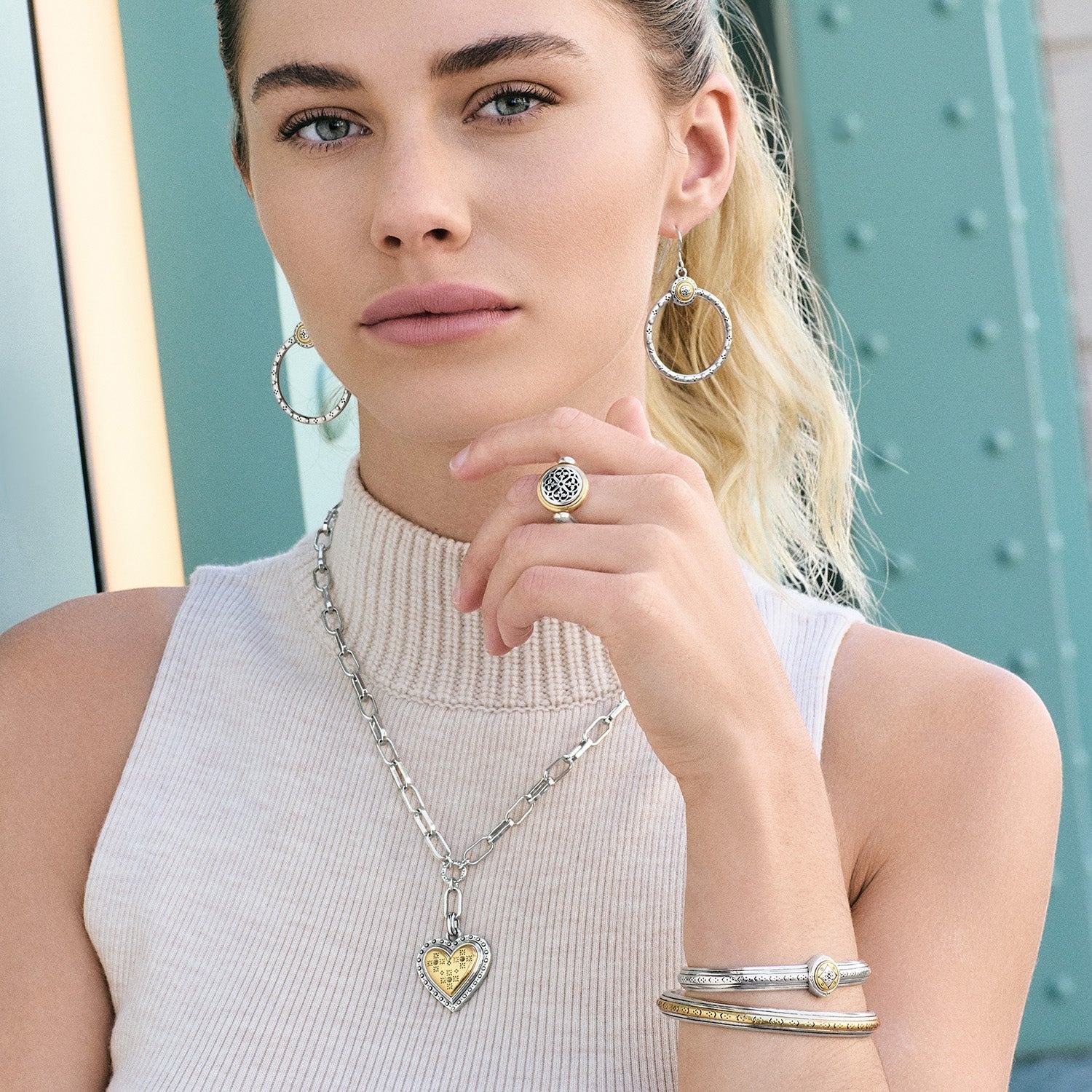 Woman wearing silver hoop earrings, a ring, and bracelets with a neutral background