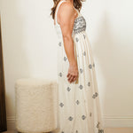 Woman wearing a long, white dress with black patterns in a room.