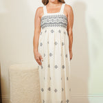 Woman wearing a white dress with black patterns standing against a plain background