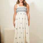 Woman wearing a white dress with black patterns in a room.