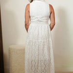 Woman wearing a white lace dress standing against a plain wall.