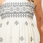 Woman wearing a white dress with black patterns in a room.