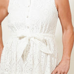 Woman wearing a white sleeveless dress standing against a plain background