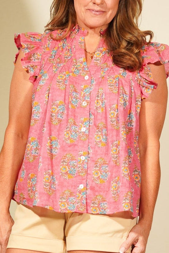 Woman wearing a pink floral blouse and beige shorts standing in a room with a mirror and chair.