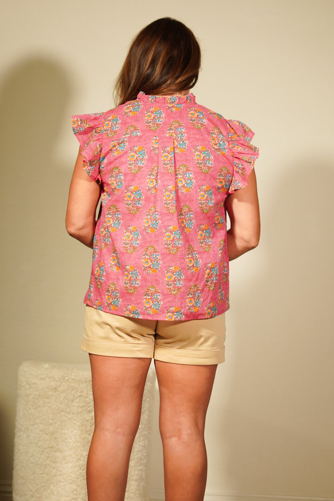 Person wearing a pink floral sleeveless top and beige shorts against a plain background