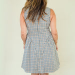 A woman modeling a sleeveless high-neck A-line dress with a blue, white, and beige gingham check pattern, standing against a plain cream-colored background.
