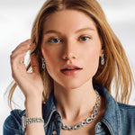 Woman wearing silver jewelry including earrings and a necklace, with a plain background
