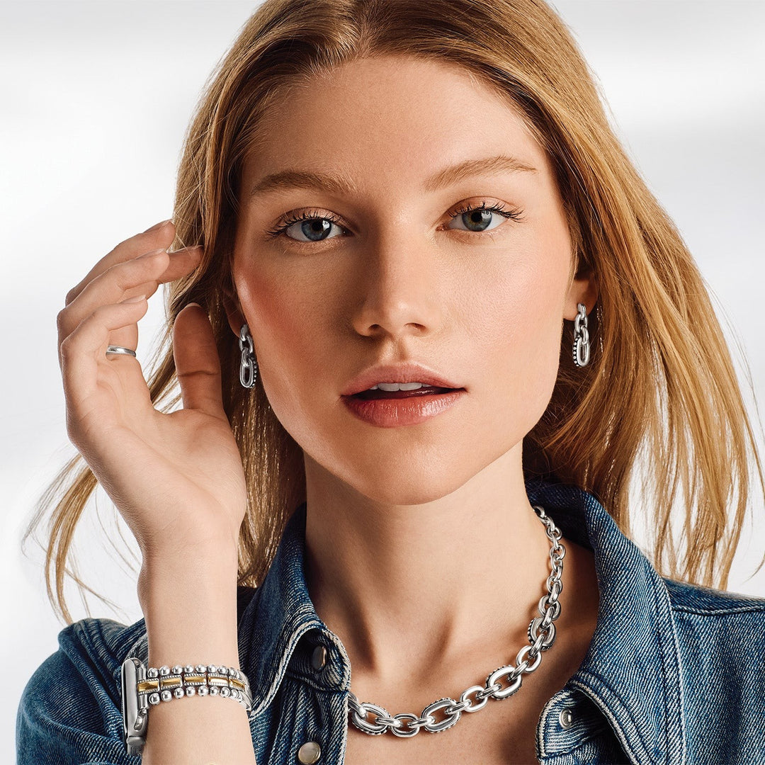 Woman wearing silver jewelry including earrings and a necklace, with a plain background