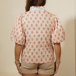 Person wearing a pink patterned shirt and beige shorts standing in front of a mirror.