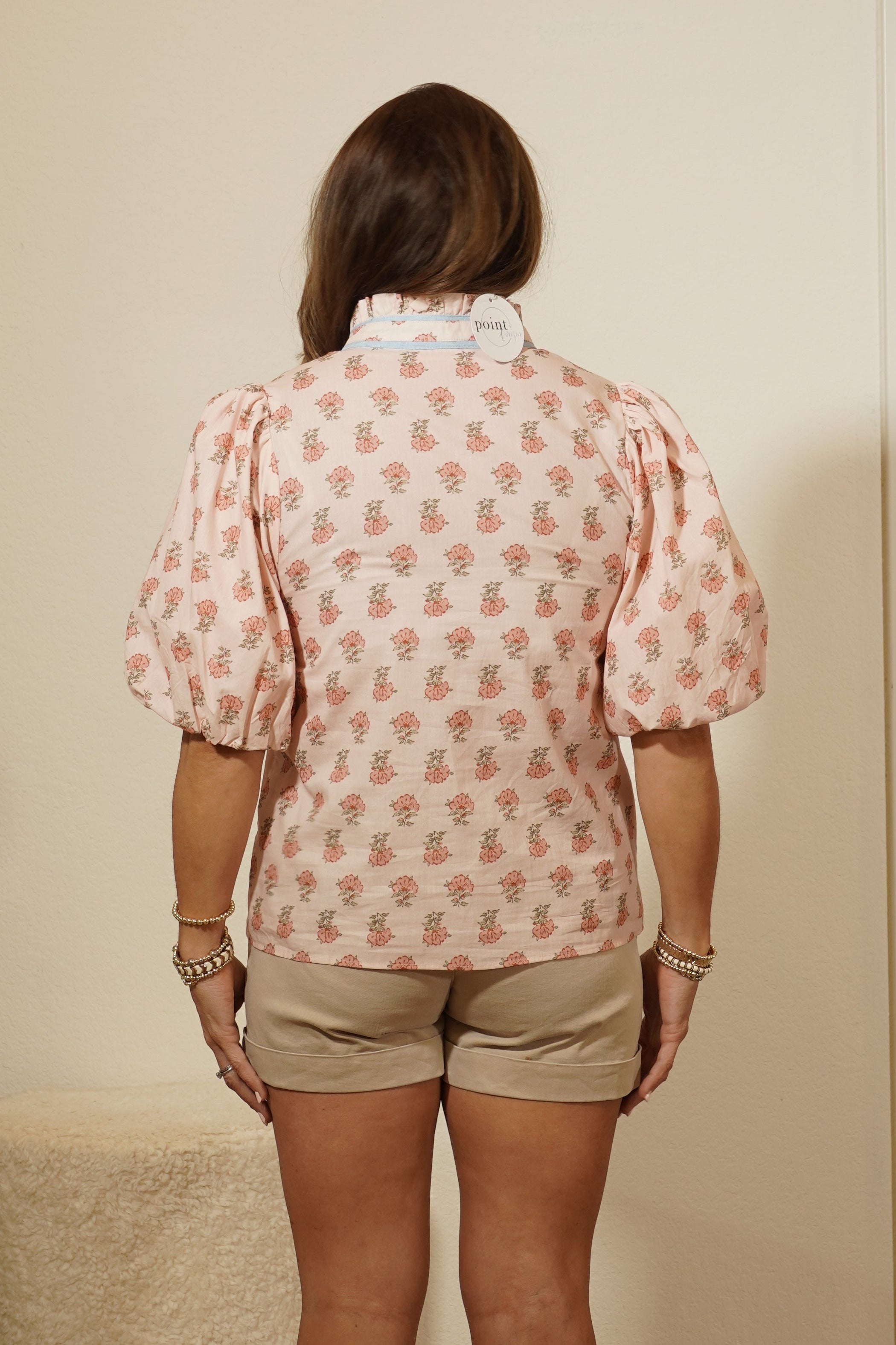 Person wearing a pink patterned shirt and beige shorts standing in front of a mirror.