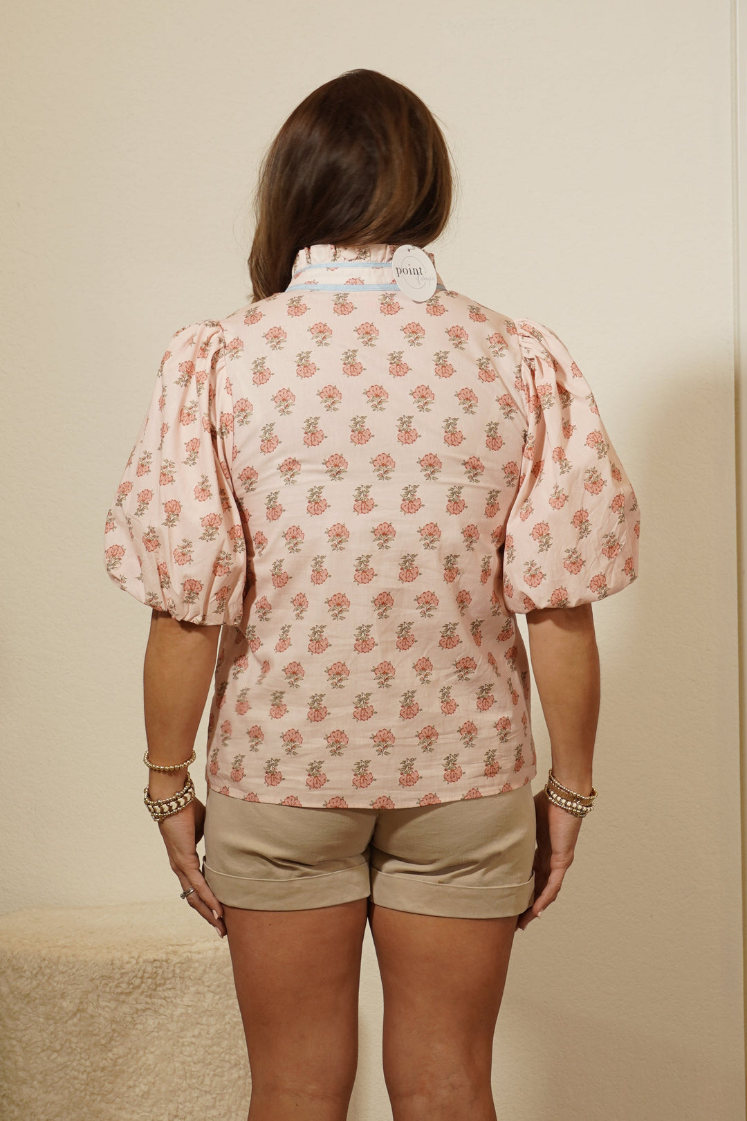 Person wearing a pink patterned shirt and beige shorts standing in front of a mirror.