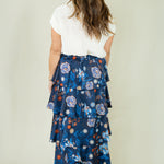 Woman wearing navy floral tiered ruffle maxi skirt with white top from the back view