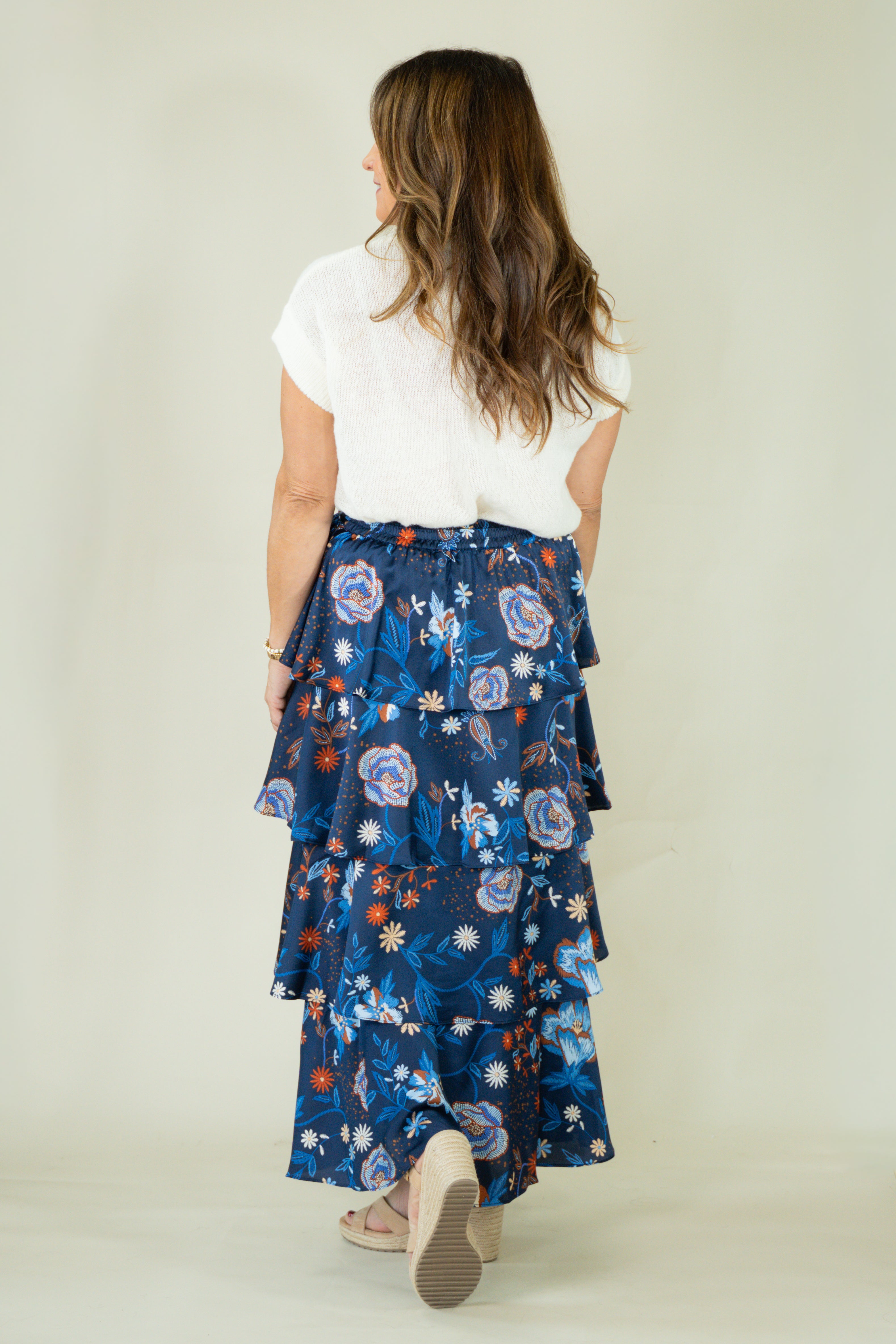 Woman wearing navy floral tiered ruffle maxi skirt with white top from the back view