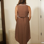 Person wearing a polka dot dress standing in front of a mirror in a room.