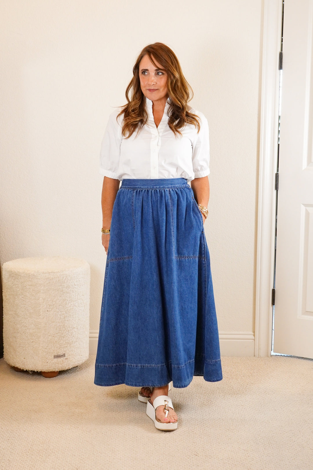 Woman wearing a white blouse and blue skirt in a room with a dresser and mirror.