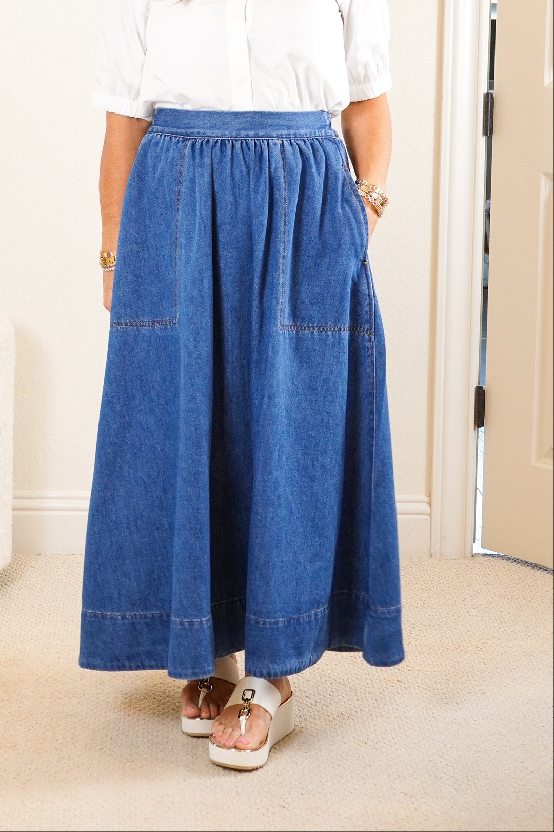 Woman wearing a white blouse and blue denim skirt in a room with a mirror and dresser.
