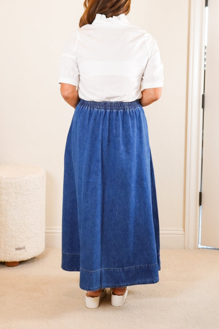 Person wearing a blue skirt and white top in a bedroom setting.