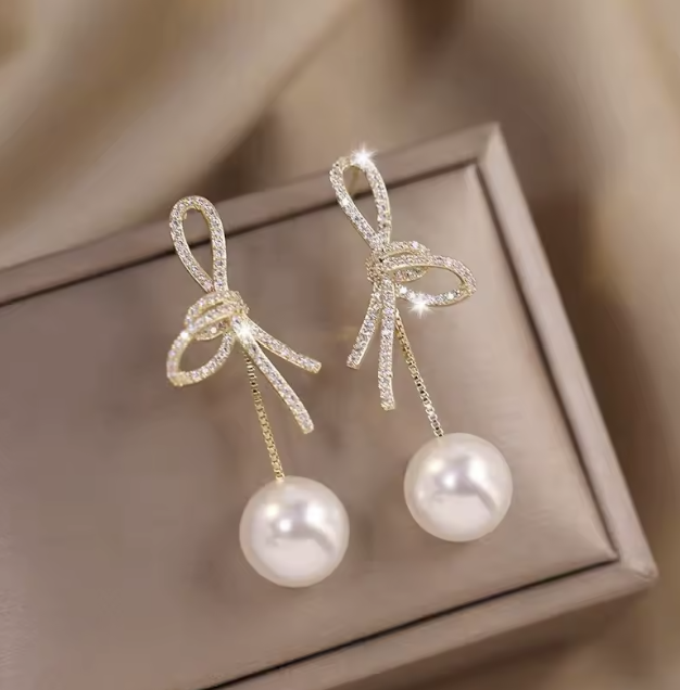 Bow-shaped earrings with pearls on a beige box