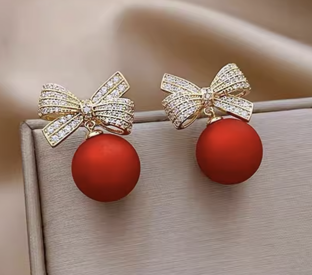 Earrings with gold bow and red ball design on a neutral background