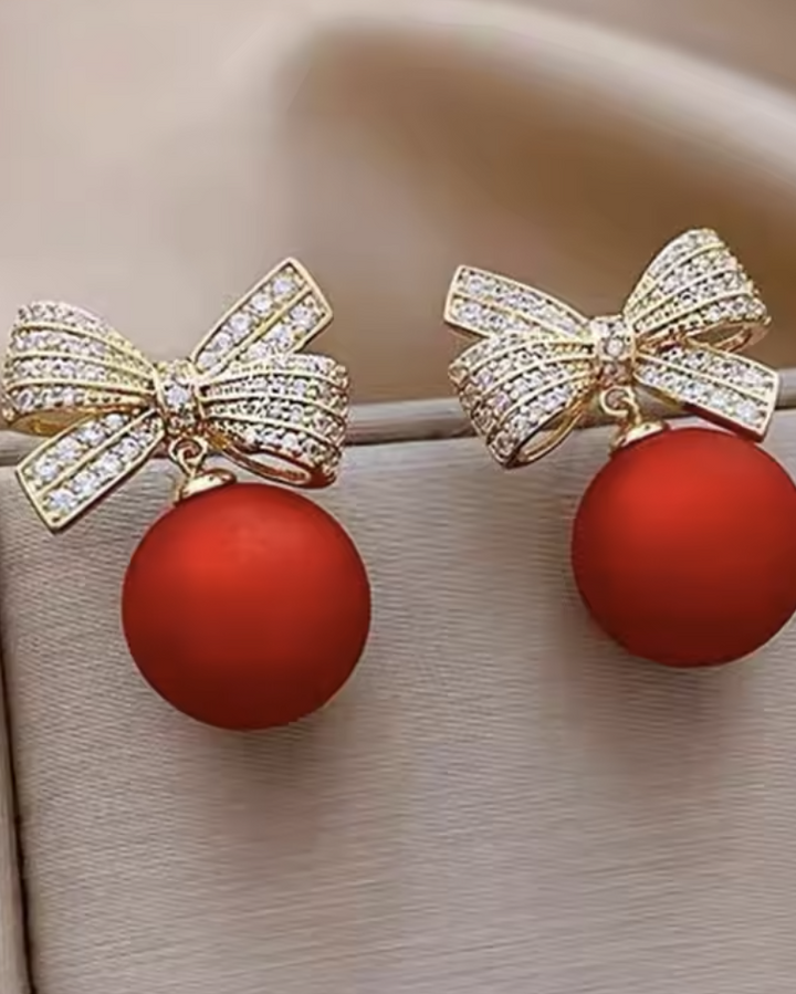 Earrings with gold bow and red ball design on a neutral background