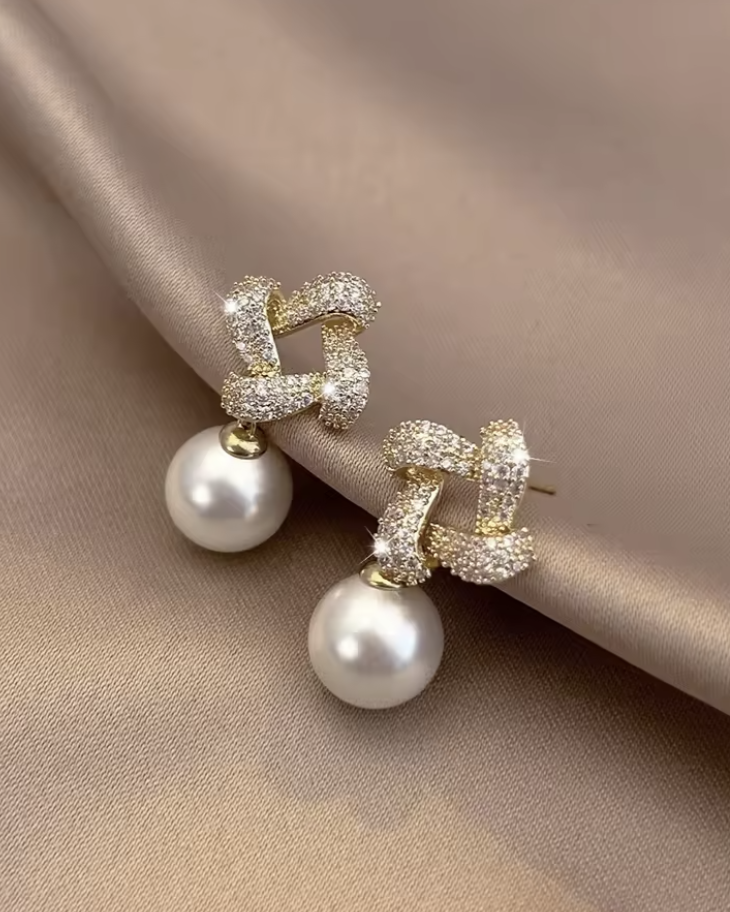 Pair of earrings with pearl drops and gold accents on a beige fabric background