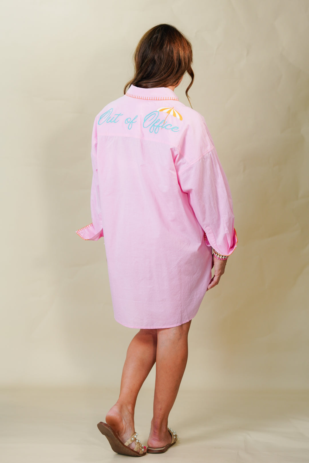 Person wearing a pink dress with text on the back against a beige background