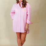Woman wearing a pink dress with colorful trim against a plain background