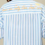 Person wearing a blue and white striped dress with text on the back against a beige background