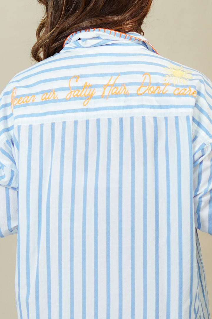 Person wearing a blue and white striped dress with text on the back against a beige background