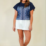 Woman wearing a navy blue top with white pattern and white shorts on a beige background
