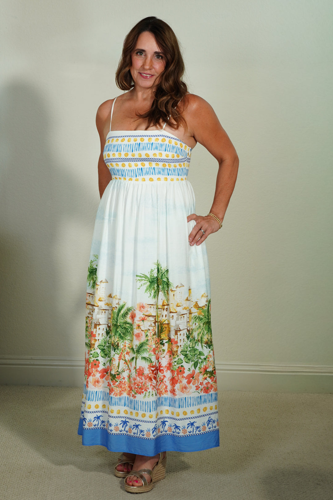 Woman wearing a colorful dress with floral and beach scene design against a plain background