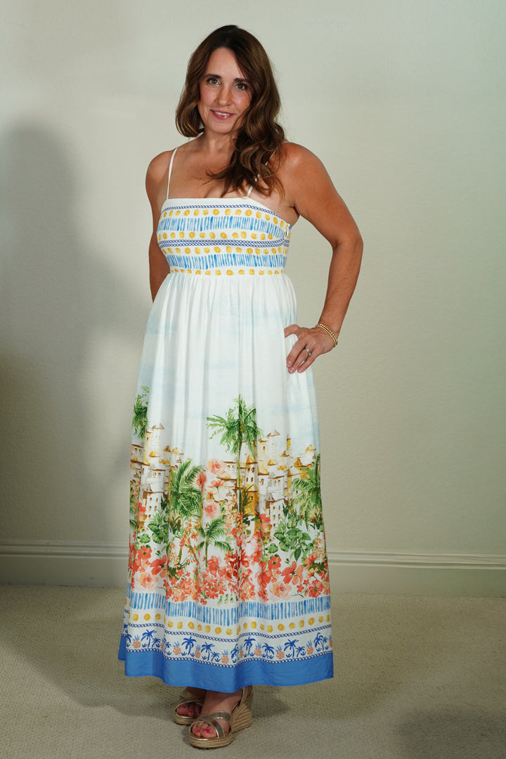 Woman wearing a colorful dress with floral and beach scene design against a plain background