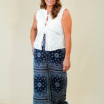 Woman wearing a white sleeveless top and blue patterned pants against a plain background